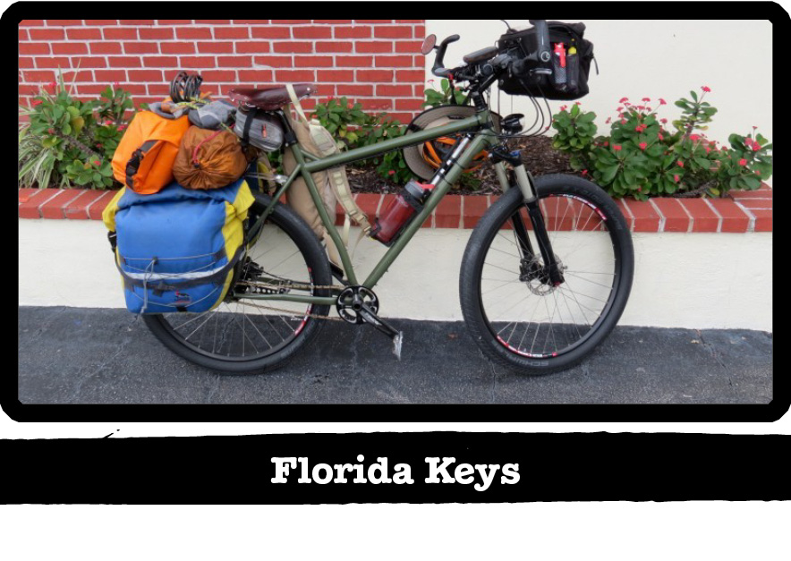 Right side view of a Surly bike, green, loaded with gear, in front of a red brick wall - Florida Keys tag below image