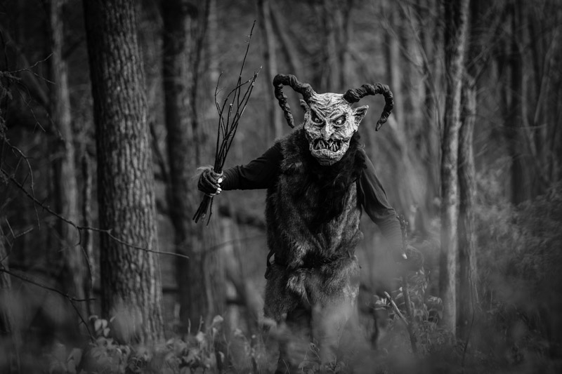 Front view of a person in a Krampus costume in the forest - black and white image