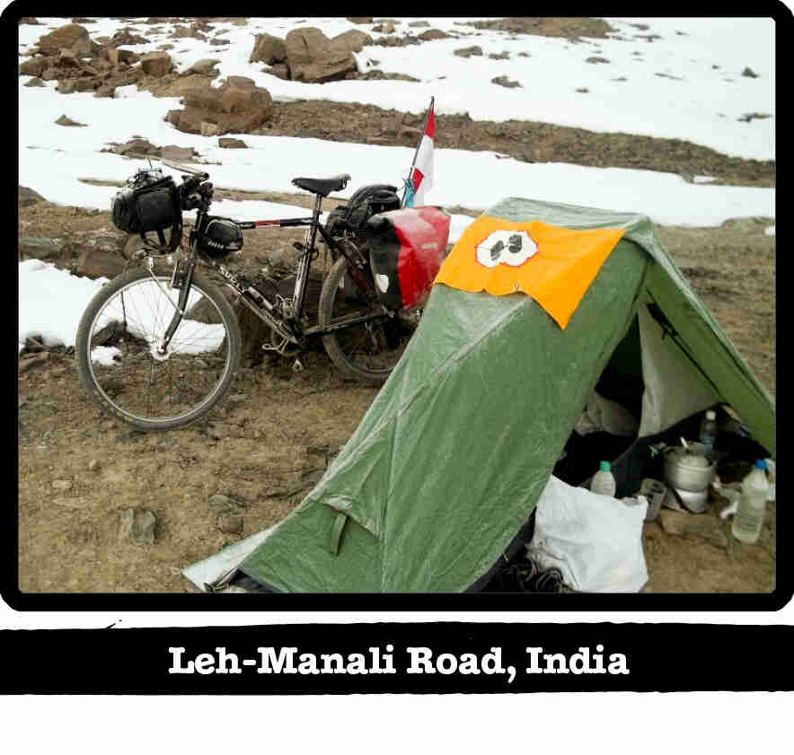 Surly Long Haul Trucker bike with gear, leaning on a rock behind a tent in the snowy mountains - Leh-Manali Road, India banner below image