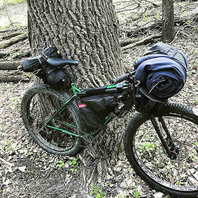 Right side view of a green Surly bike loaded with gear, parked against the base of a tree
