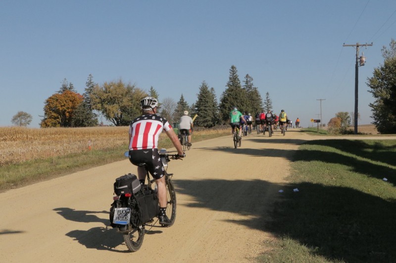 Rear view of a cyclist riding a Surly Big Dummy bike down a gravel road in the country, with a group of cyclists ahead
