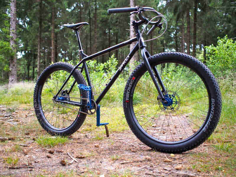 Right side view of a black Surly bike with Chupacabra tires, parked in a forest clearing