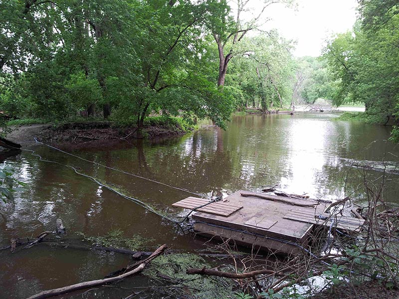 A wood deck raft, in a river and next to the bank