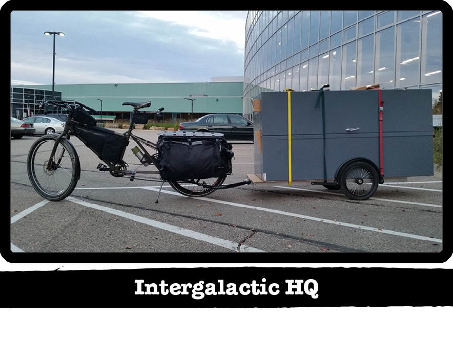 Left side view of a Surly Big Dummy bike with a trailer behind, on a parking lot - Intergalactic HQ tab below the image