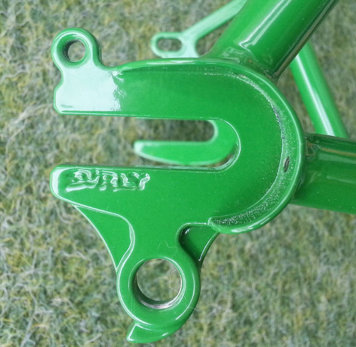 Downward, close up, right side view of the dropout detail of a green Surly bike frame, with grass below it