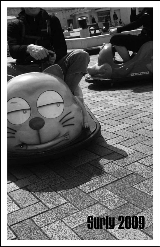 Surly Bikes - 2009 Catalog Cover - Black & White photo of a person driving a bumper car with a cat face on the front
