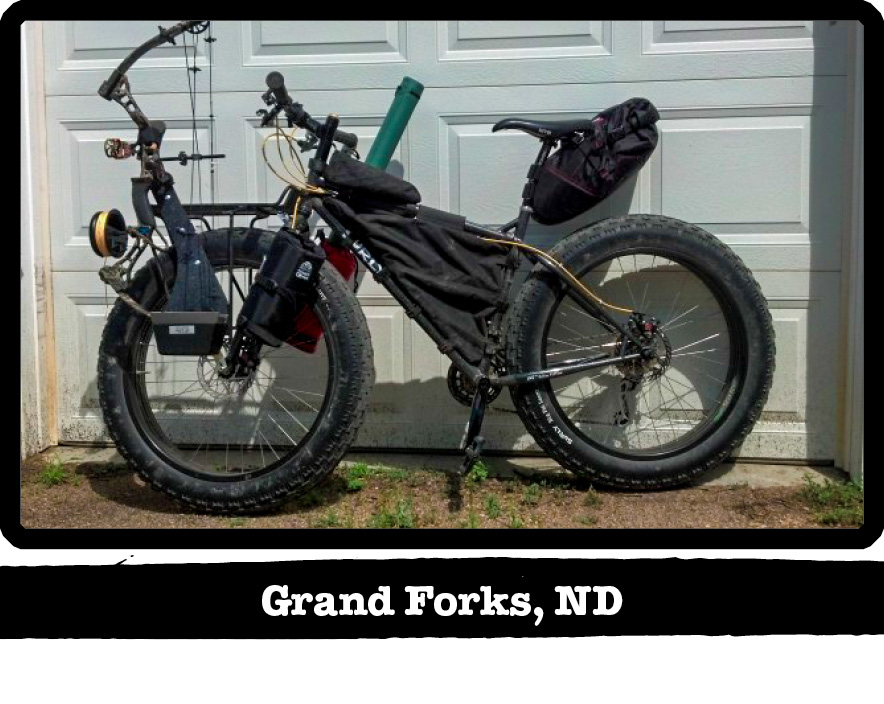 Left side view of a Surly fat bike, black, with a bow on front, against a garage door - Grand Forks, ND tag below image