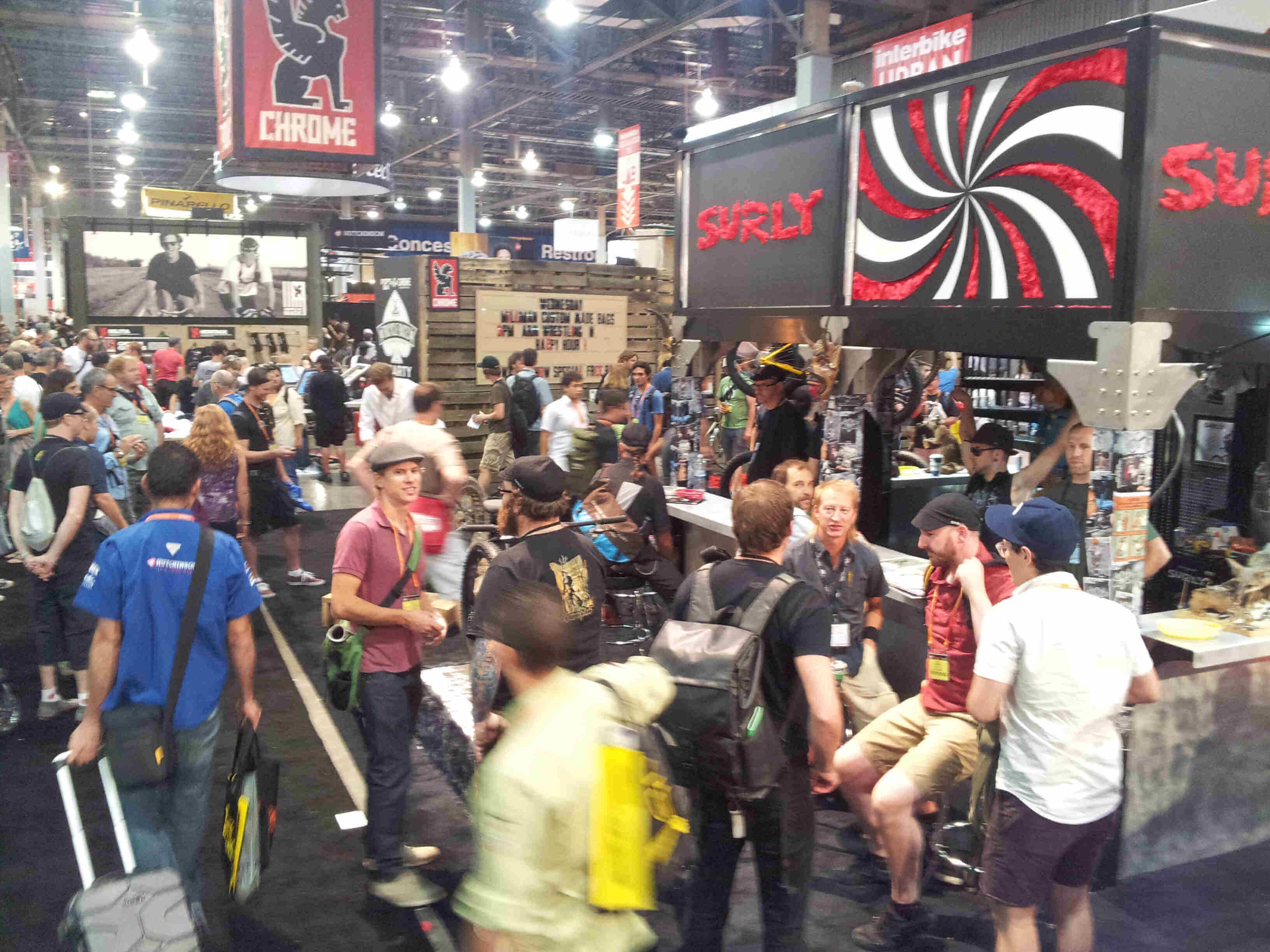 A large gathering people inside of an event center, next to the Surly Bikes display booth
