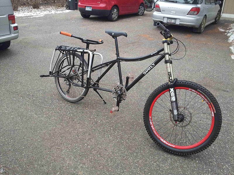 Right side view of a black Surly Big Dummy bike, standing on a paved parking lot, with vehicles behind it