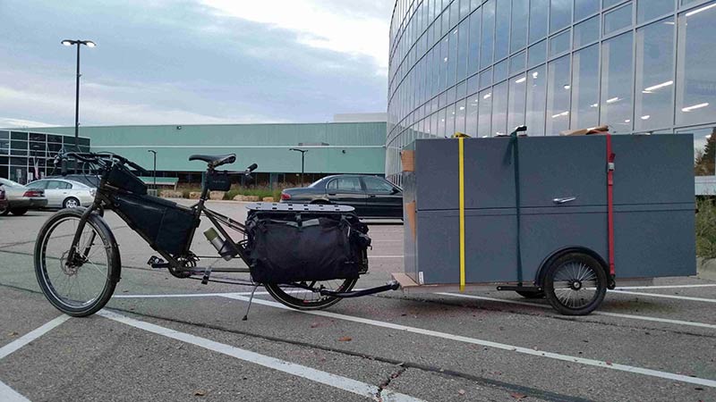 Left side view of a Surly Big Dummy bike, with a trailer loaded with cabinets, on a parking lot of an office complex