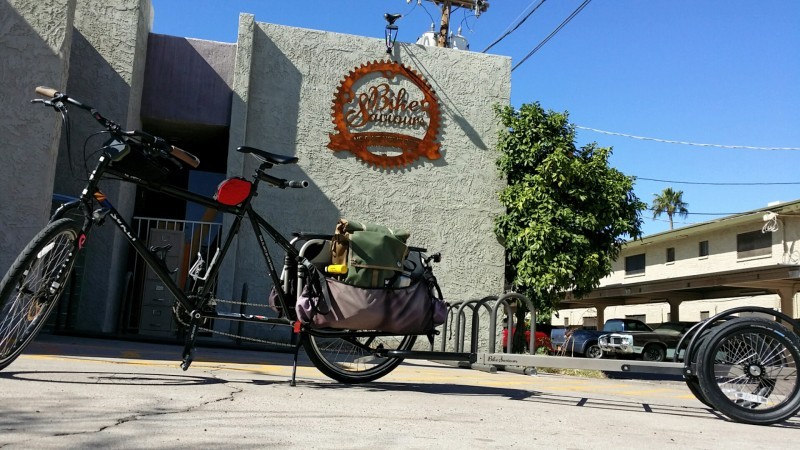 Left side view of a black Surly Big Dummy bike with a trailer, parked in front of a bike shop