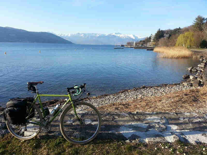 Right side view of a green Surly Cross Check bike, parked on a lakeshore, with mountains in the background