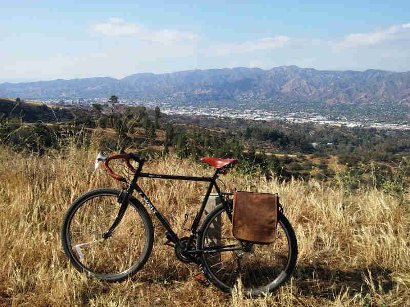 Left side view of a black Surly Cross Check bike parked in grass on a hilltop, with mountains in the background
