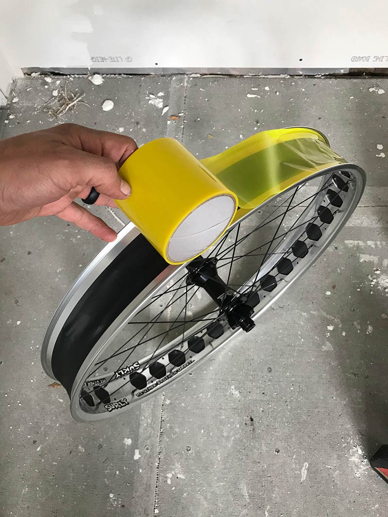 Downward view a hand applying yellow tubeless tape around a Surly fat bike rim standing upright