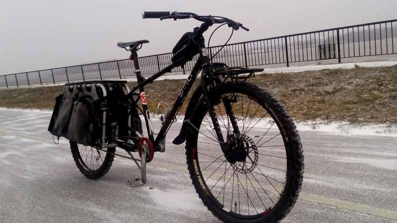 Front right side view of a black, Surly Troll bike, in the middle of an icy road, with a fence in the background