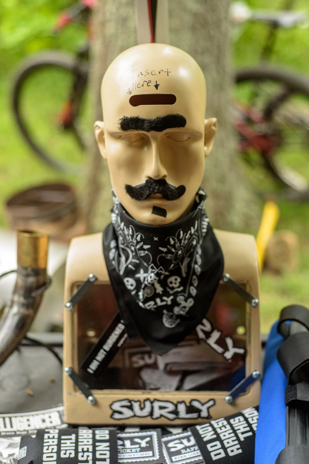 Chest up part of mannequin with a unibrow, mustache and black bandana around the next on a table with a Surly sticker 