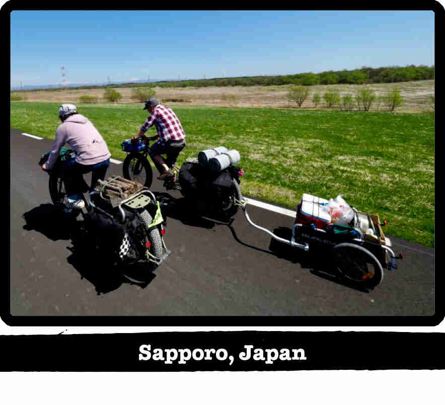 Rear view of 2 cyclists riding Surly fat bikes on a remote paved road - Sapporo, Japan tag below image