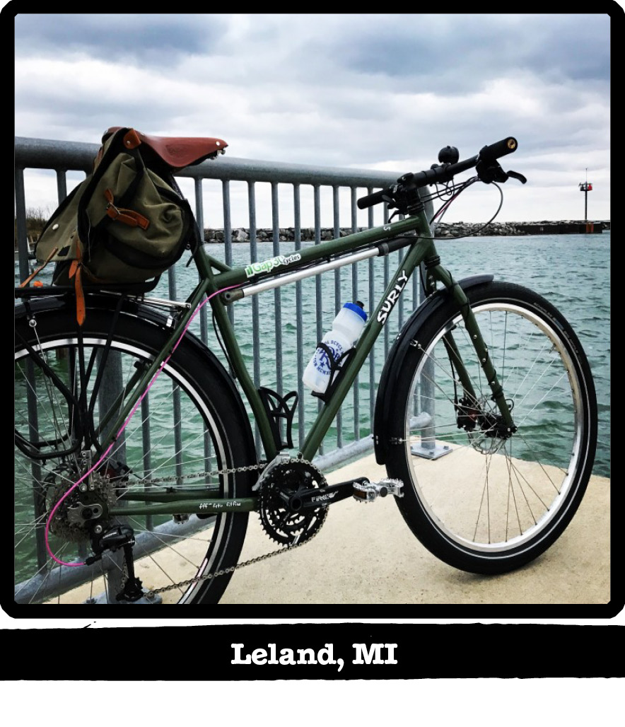 Right side view of a green Surly bike against a rail on a dock facing a waterway-Leland, MI banner shown below image