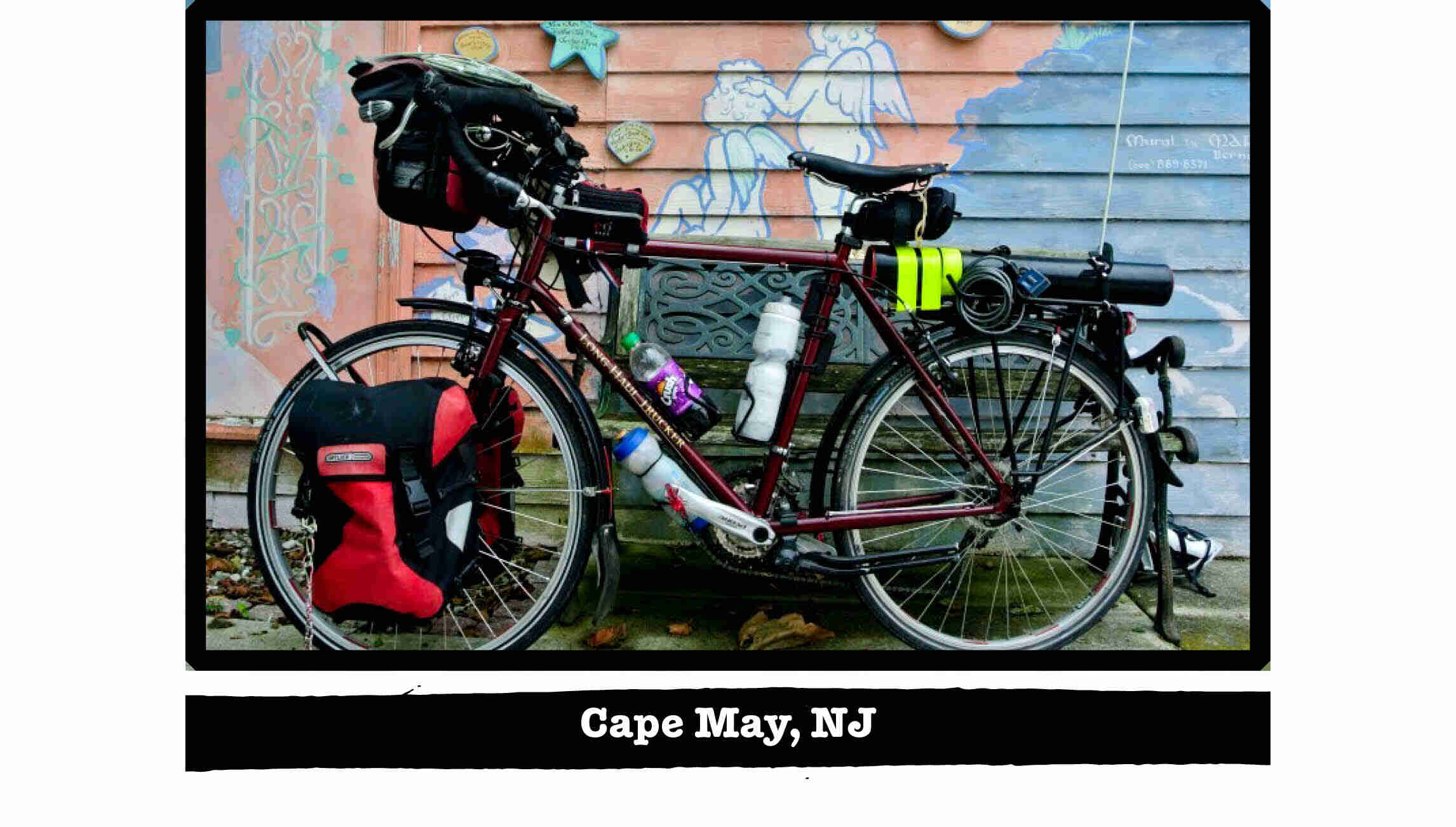 Left side view of a Surly Trucker bike, loaded with gear, in front of a wall with a mural - Cape May, NJ tag below image