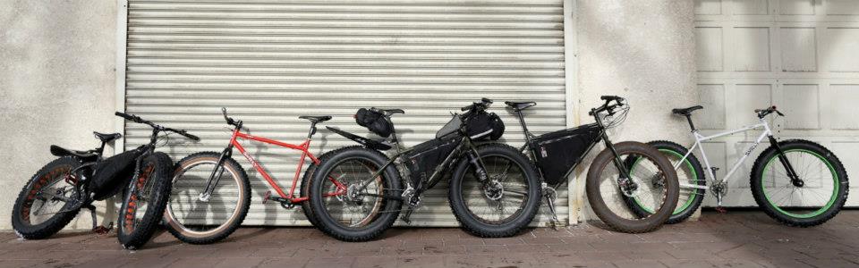 Side view of Surly fat bikes, leaning against the outside of 2 large, white, garage doors