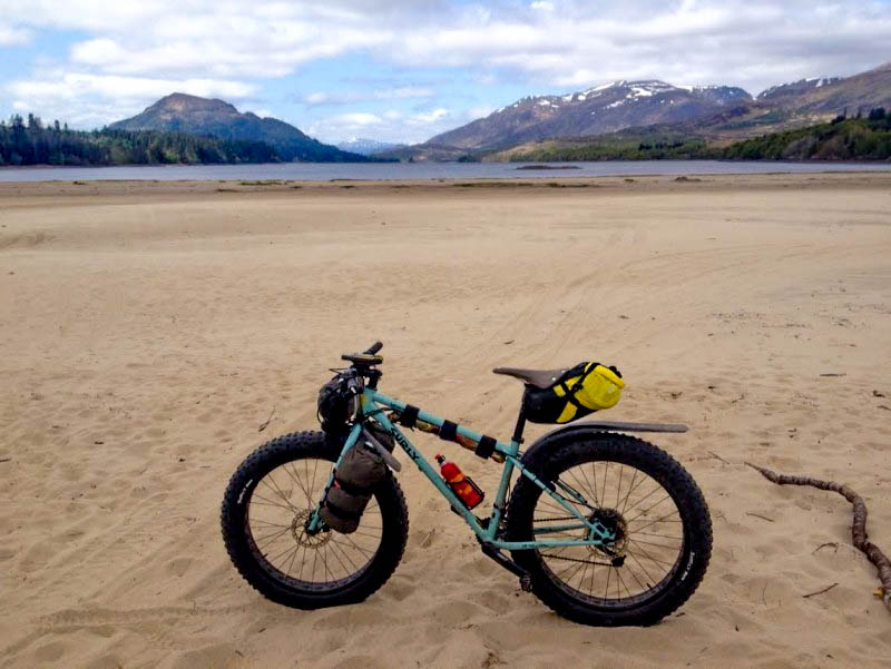 Left side view of a Surly Wednesday MY17 fat bike, in a field of sand, with a lake and mountains in the background