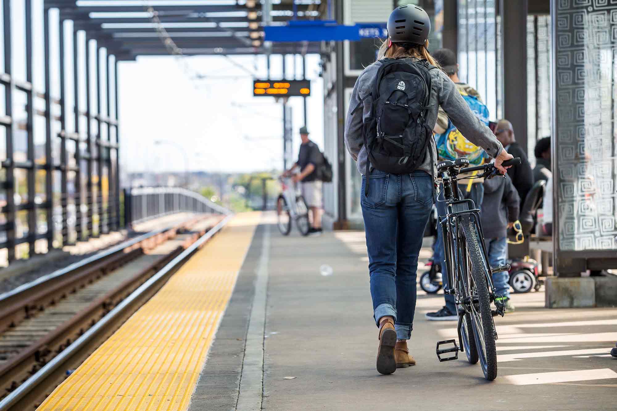 バックパックとヘルメットを身につけ、自転車で通勤電車のホームまで歩くサイクリスト