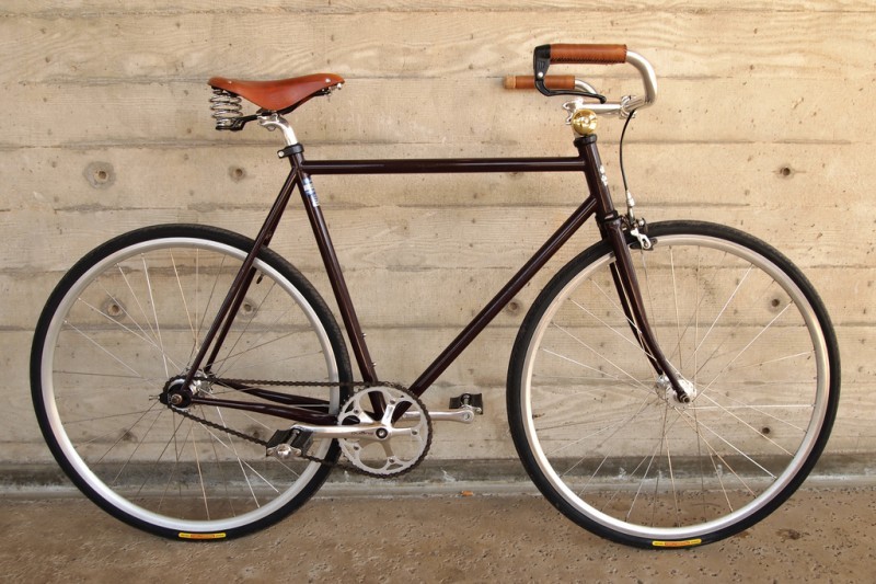 Right side view of a brown Surly bike, with a leather seat and grips, leaning against a cement wall