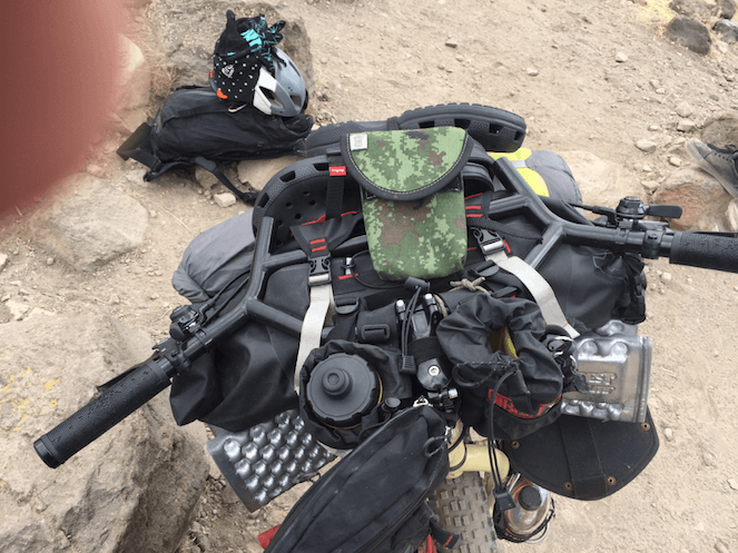 Downward view of the handlebar loaded with gear, on a bike on rocky gravel