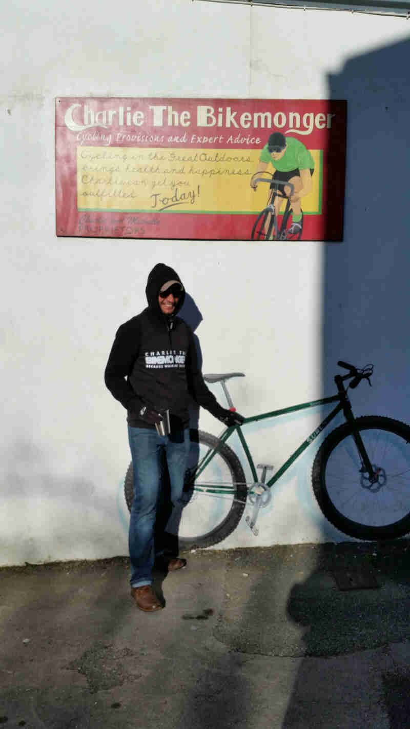 Front view of person standing against a while wall with a bike and sign painted on it