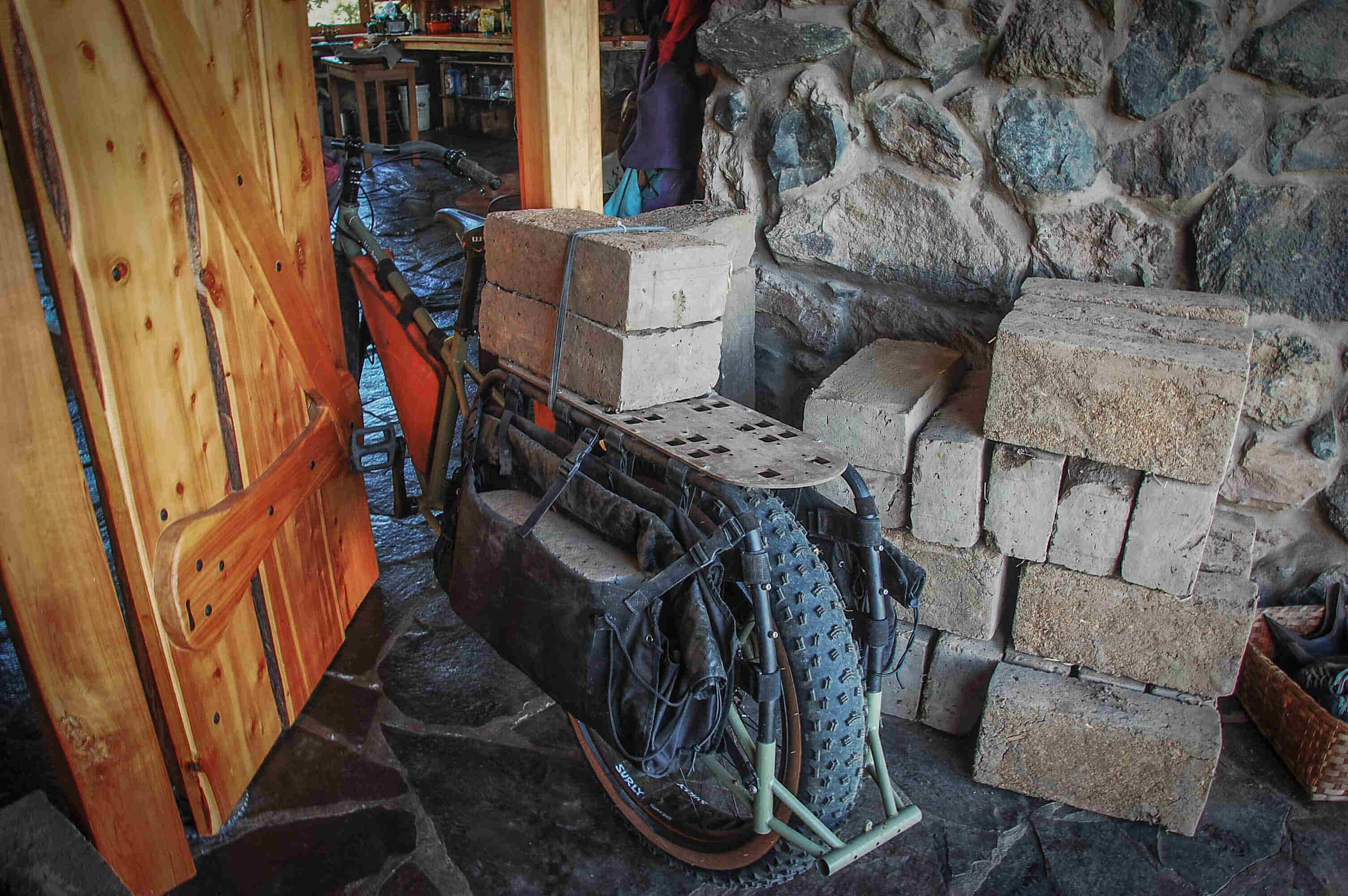 Left rear view of a Surly Big Fat Dummy bike with cement blocks on the rear rack, in the doorway of a stone building