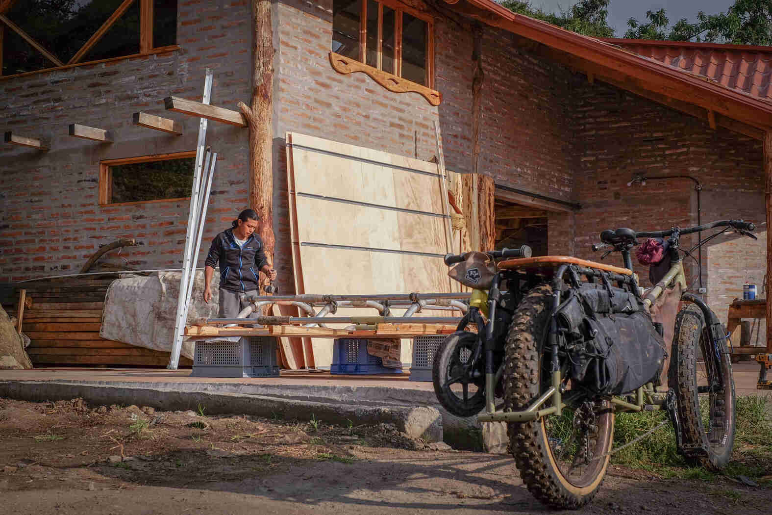 Rear ride side view of a Surly Big Fat Dummy bike, with a people building a structure in front of a brick house
