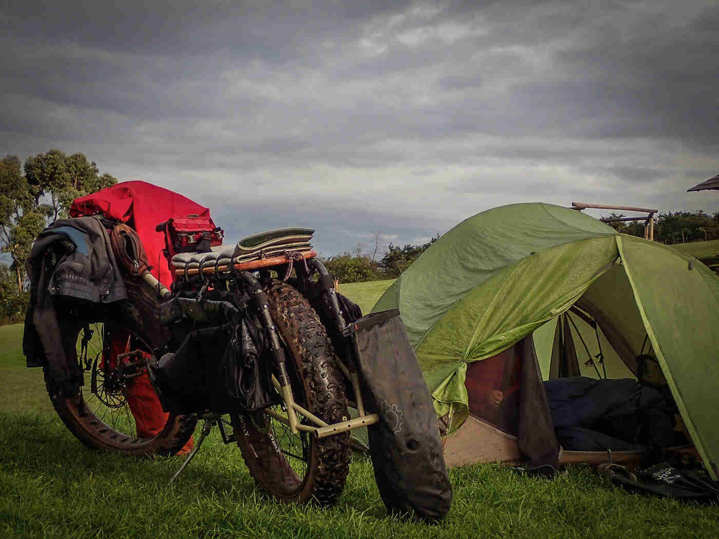Rear view of a Surly Big Fat Dummy bike next to a green tent, in a grass field, with dark, gray clouds above