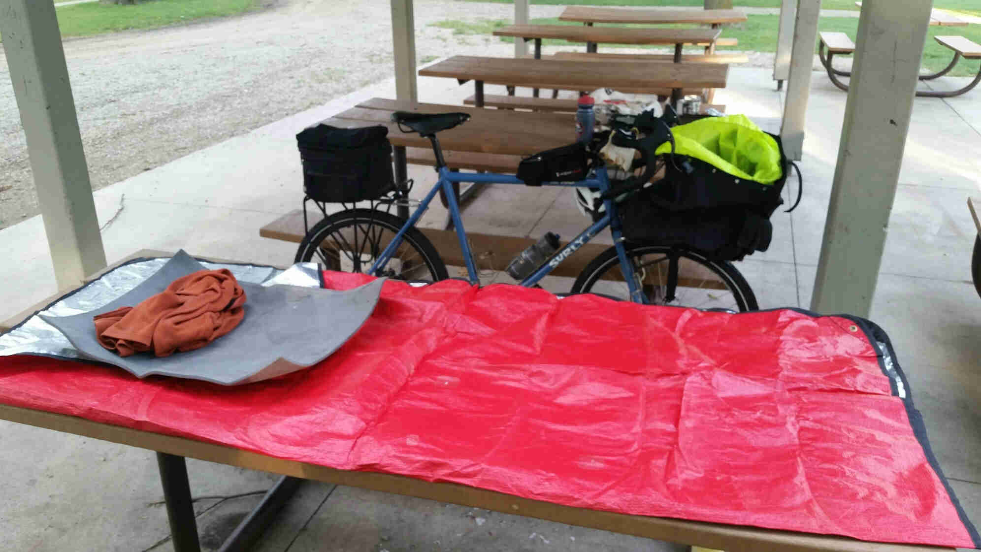 Red tarp laying across a picnic table, with a Surly bike behind it, and row of picnic tables in the background