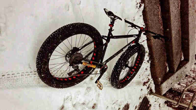 Rear view of a black Surly fat bike, laying in the snow, next to a bottom stair