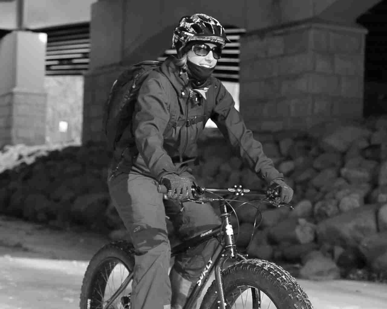 Front, right side view of a cyclist in winter attire, riding a Surly Moonlander fat bike on snow - black & white image