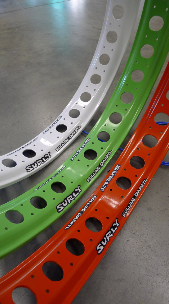 Downward, inner view of 3 Surly Rolling Darryl fat bike rims in white, green & red, standing side by side on cement