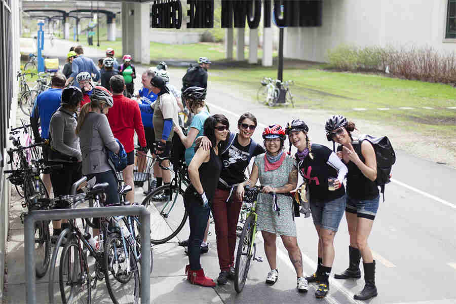 A group of cyclists with their bikes, standing on the side of a two-way bike road, in front of a bike center