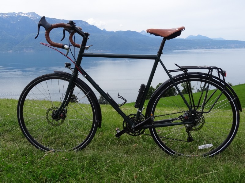 Left side view of black Surly bike, parked on a grassy hilltop, above a lake with mountains behind it