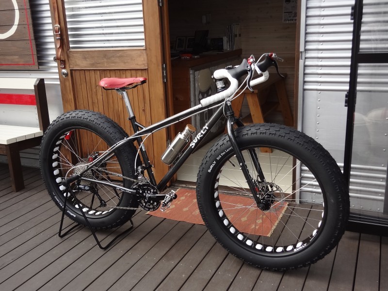 Right side view of a black Surly fat bike, parked on a deck, in front of an open door of a building with steel walls