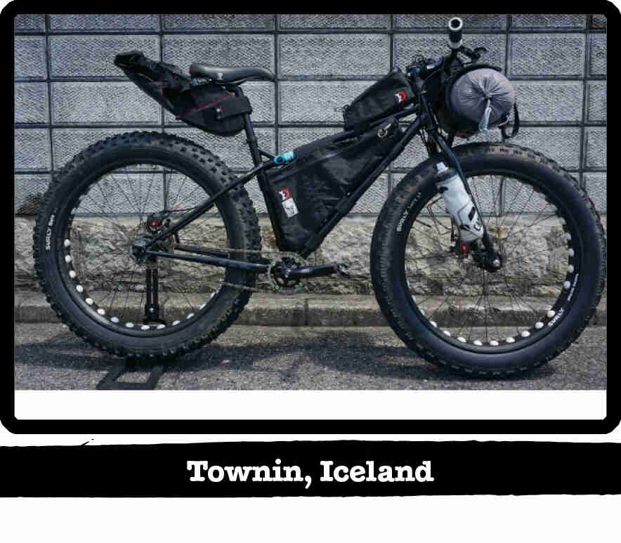 Right side view of a Surly fat bike, black, loaded with gear, on pavement  - Townin, Iceland tag below image
