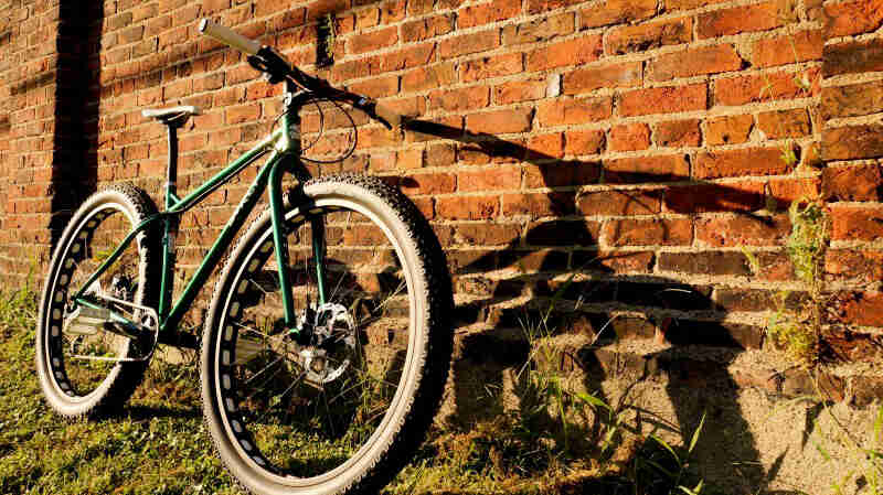 Front left side view of a Surly Krampus bike, green, leaning on a red brick wall