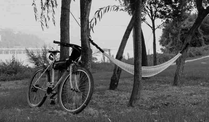 Front right side view of a Surly bike, parked in a field, against a tree with a hammock attached - black & white image
