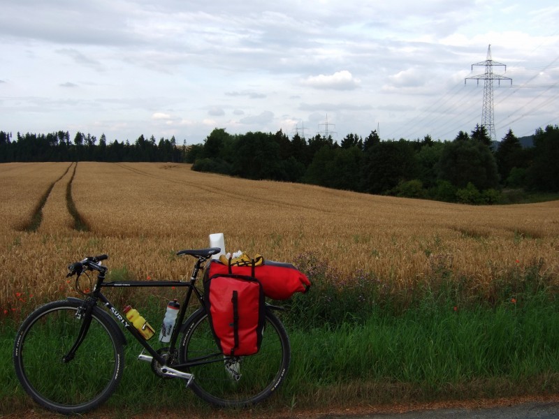 Left side view of a black Surly Cross Check bike, with gear on back, and a field of brown grass behind it