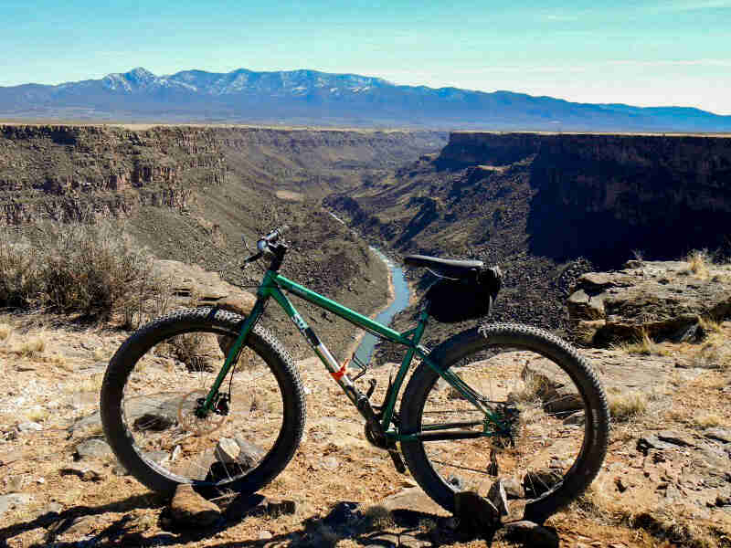 Left side view of a Surly Krampus bike, green, on the top of a river canyon, with mountains in the background