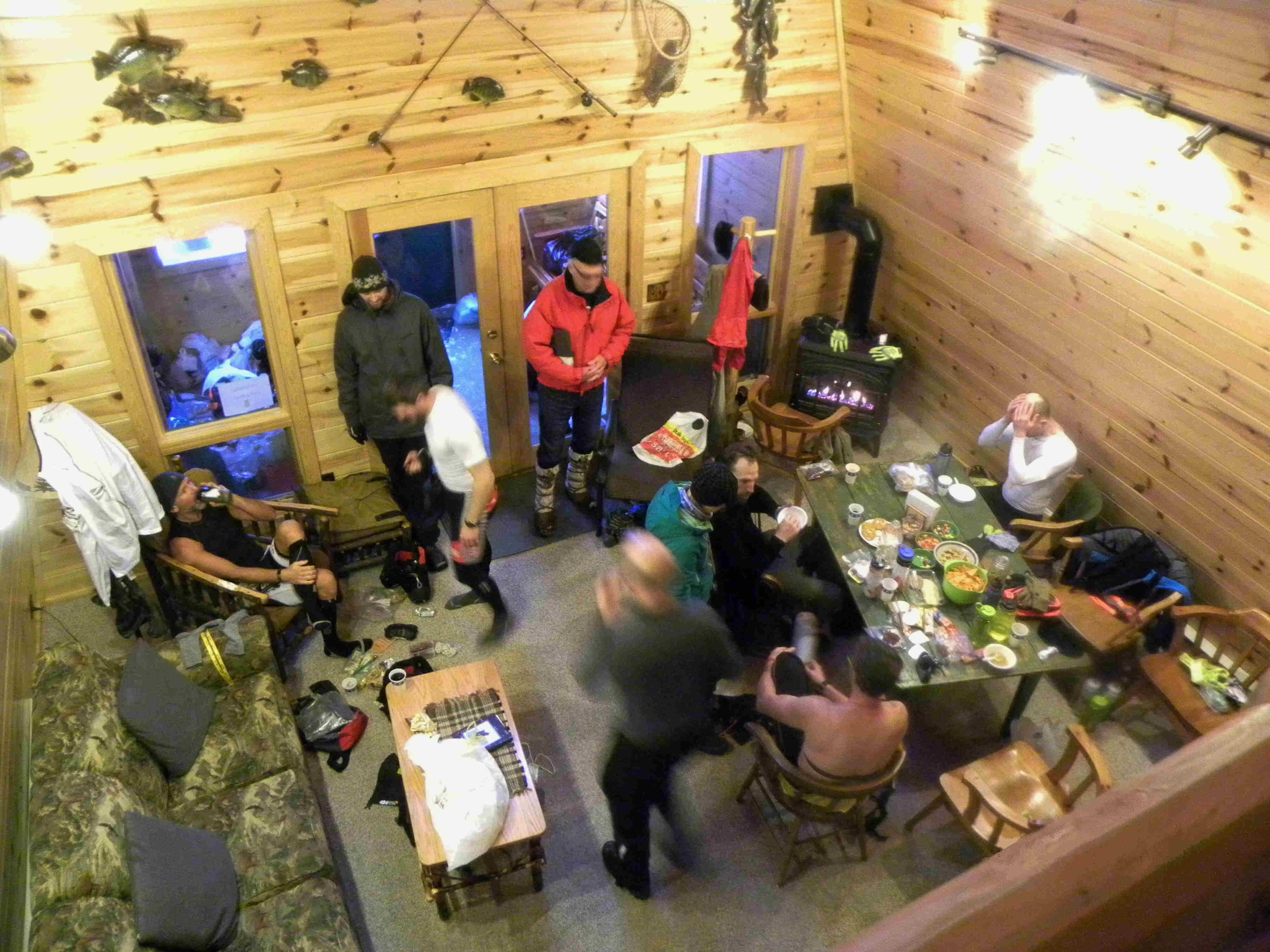 Downward view from a loft, looking down on a group of people gather inside a wood sided cabin room