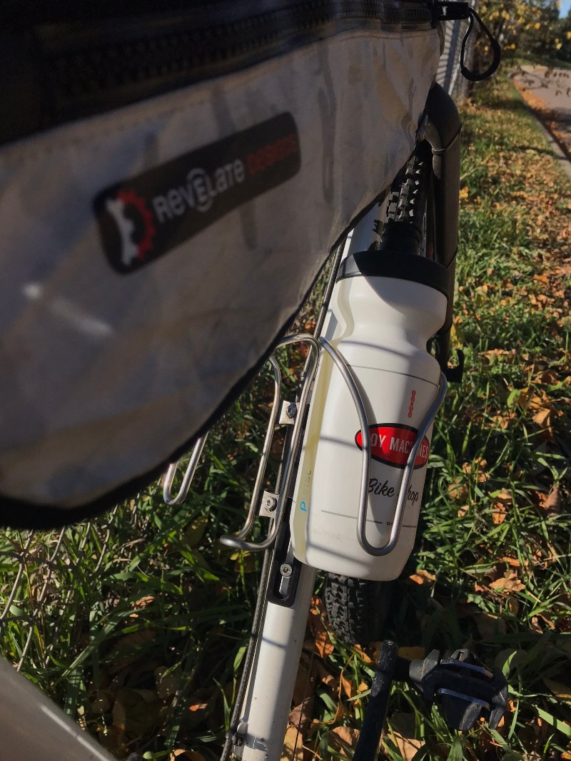A top tube gear pack and water bottle in a cage on a bike standing in the grass
