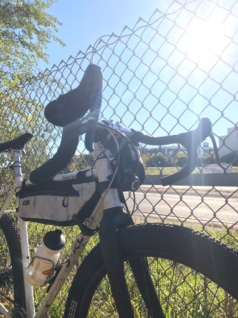 Surly Midnight Special bike leaning on a chain link fence on a sunny day next to a roadway