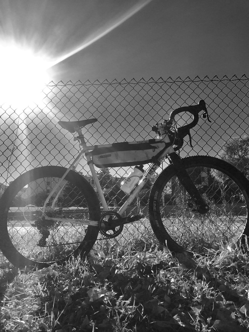 Right side view in black and white photography of a Surly Midnight Special leaning on a chain link fence in the grass