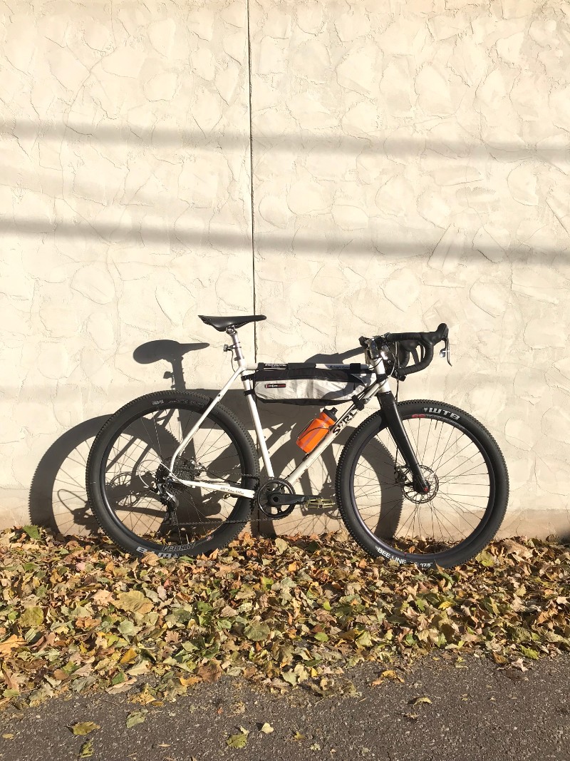 Right side view of a white Surly Midnight Special bike leaning on a tan stucco wall with leaves on the ground