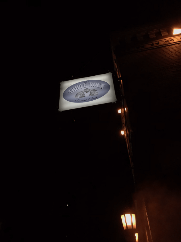 Upward side view of a Triple Rock social club sign on the outside of a building at night